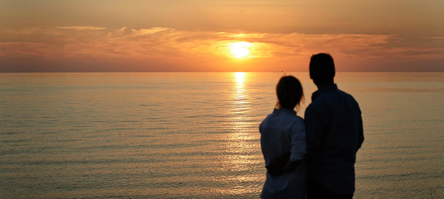 Par står og kigger ud over havet og nyder en flot solnedgang.