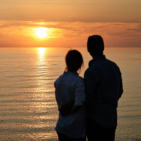 Par står og kigger ud over havet og nyder en flot solnedgang.