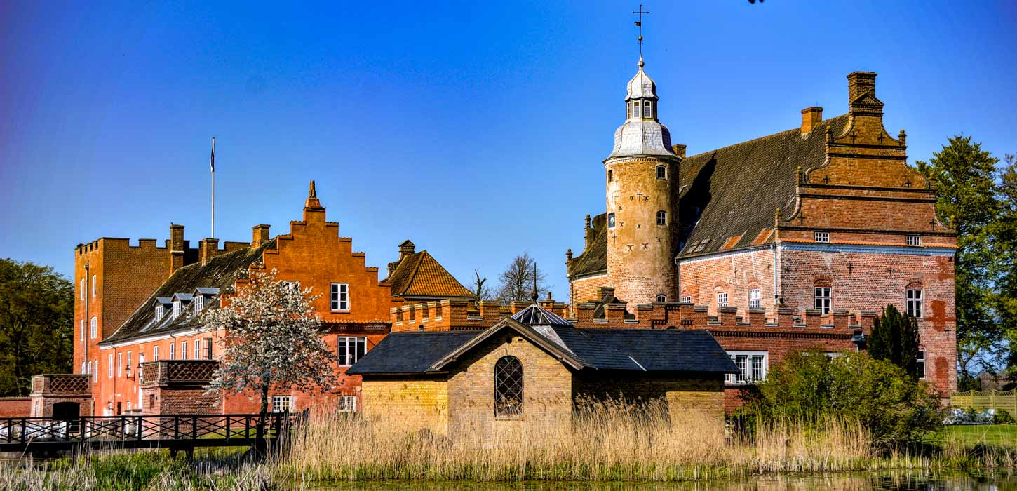 Prægtig slotsbygning i røde og gule mursten med tårn.