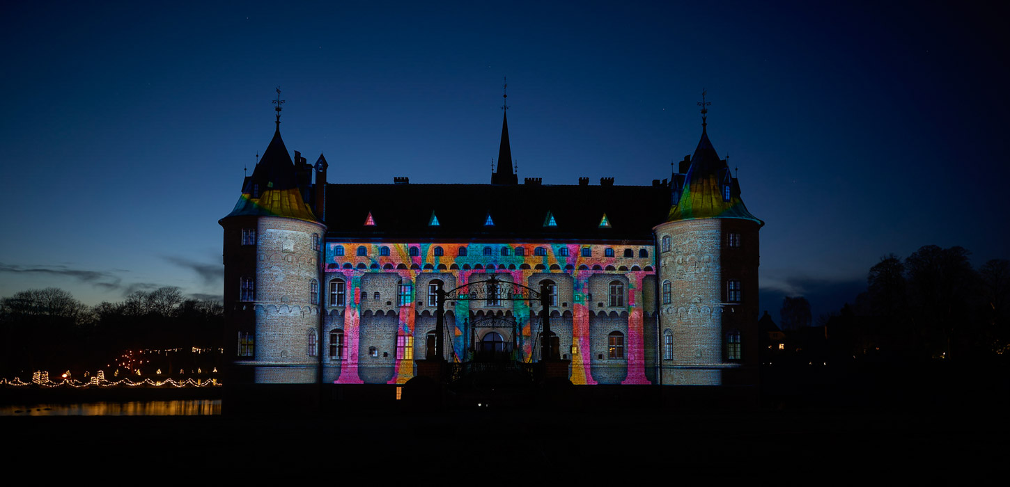 Egeskov slot ses i mørket. Facaden er lyst op i forskellig farvede mønstre.
