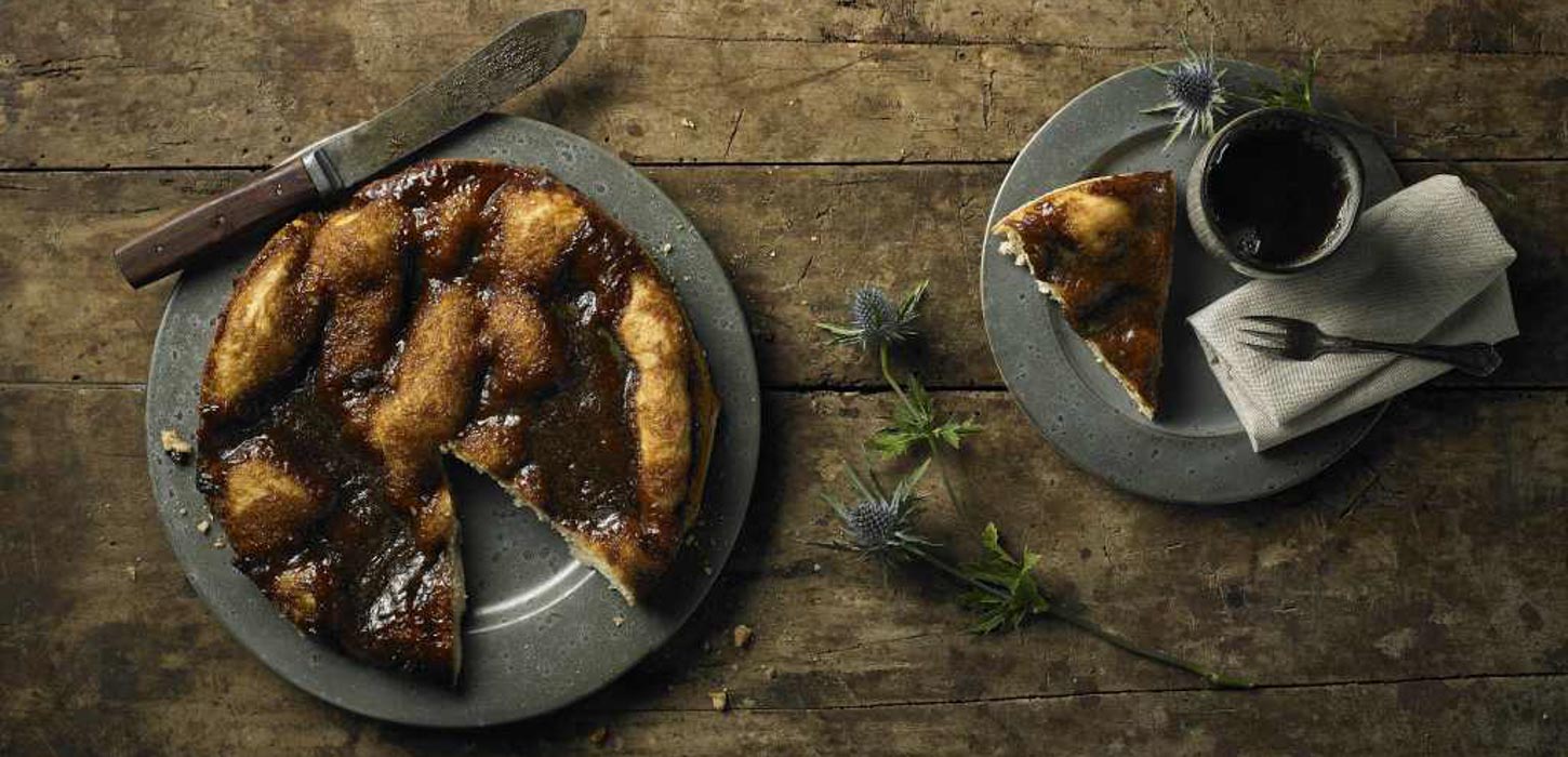 Anretning med en rundt brunsviger kage og en kop kaffe på et råt træbord set oppefra.Smag den fynske brugsviger