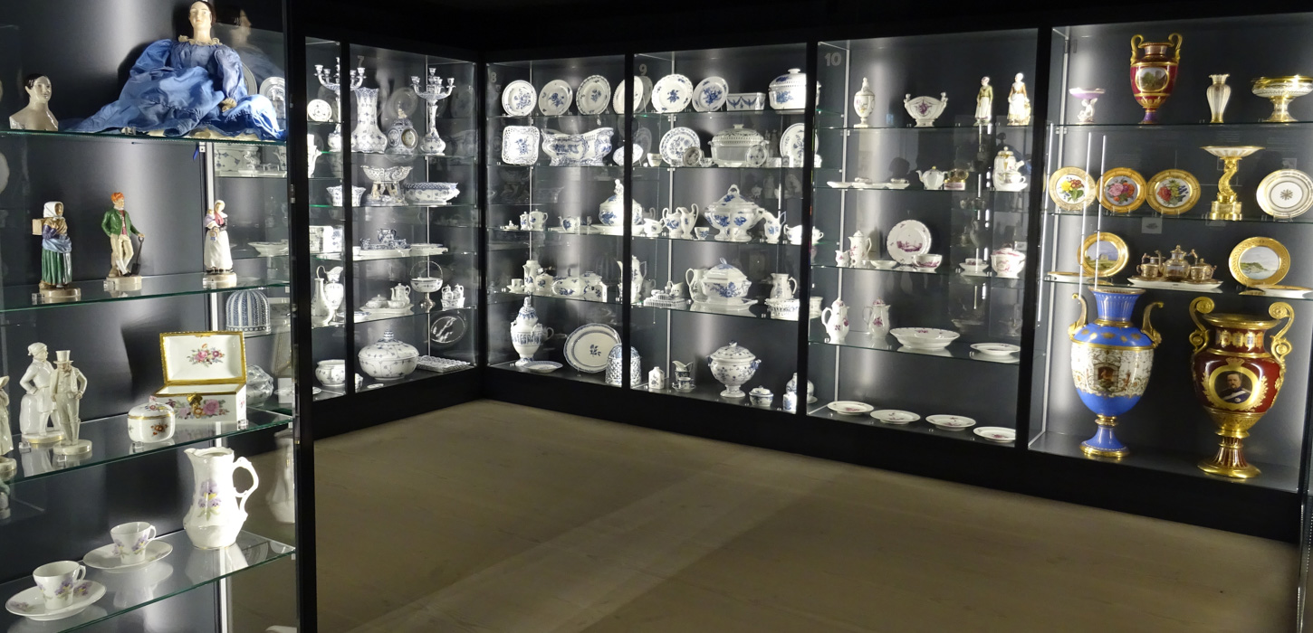 Udstillingsmontre med udstillet porcelæn på ræd og række.