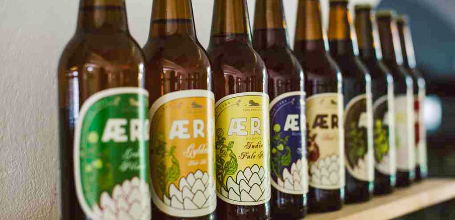 Ni brune ølflasker på række med forskellige mærkater fra Ærø Bryggeri.