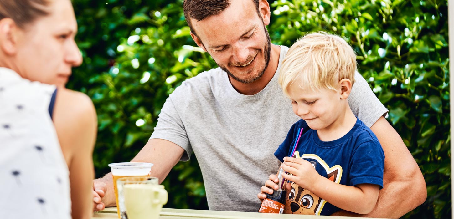 Mand sidder med bark på skødet ved et bord-bænke-sæt med en fadøl og en cola.