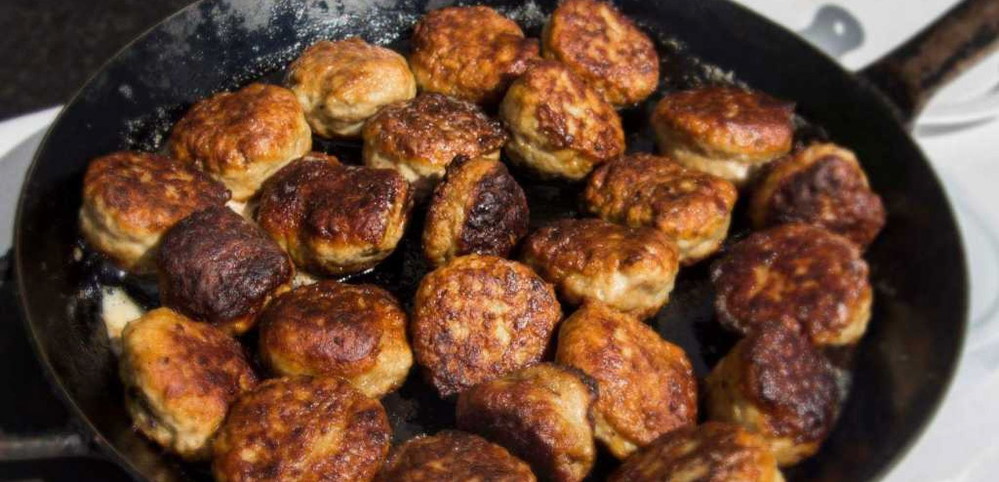 En stål stegepande fyldt med sydende frikadeller. 