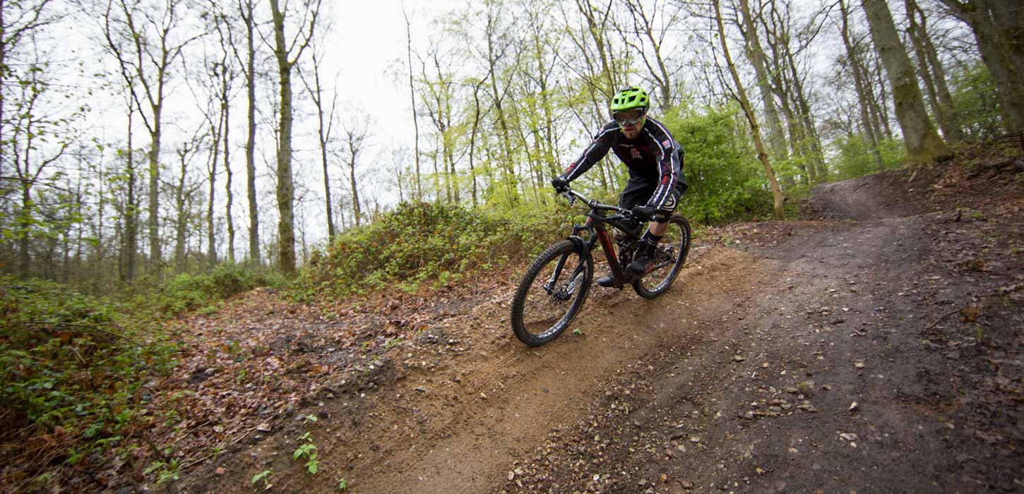 En mountainbiker med grøn hjelm cykler i skoven på vej ned ad en bakke.