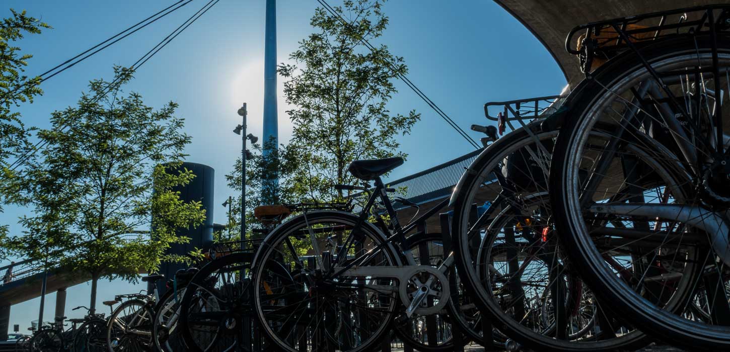 Parkerede cykler ved Byens Bro i Odense. Broen rejser sig mod en blå himmel og en bagende sol i baggrunden.