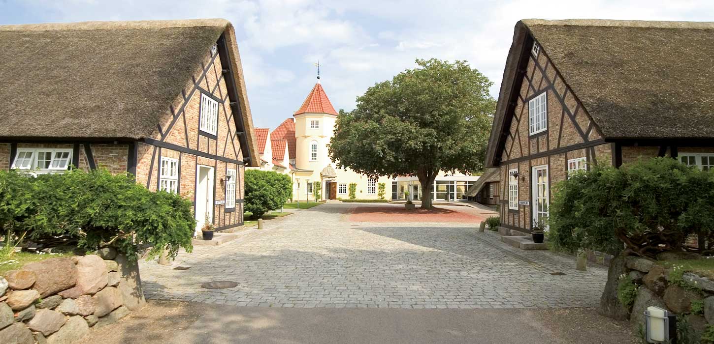 Indkørsel til hotel med to bindingsværkshuse til højre og venstre. 