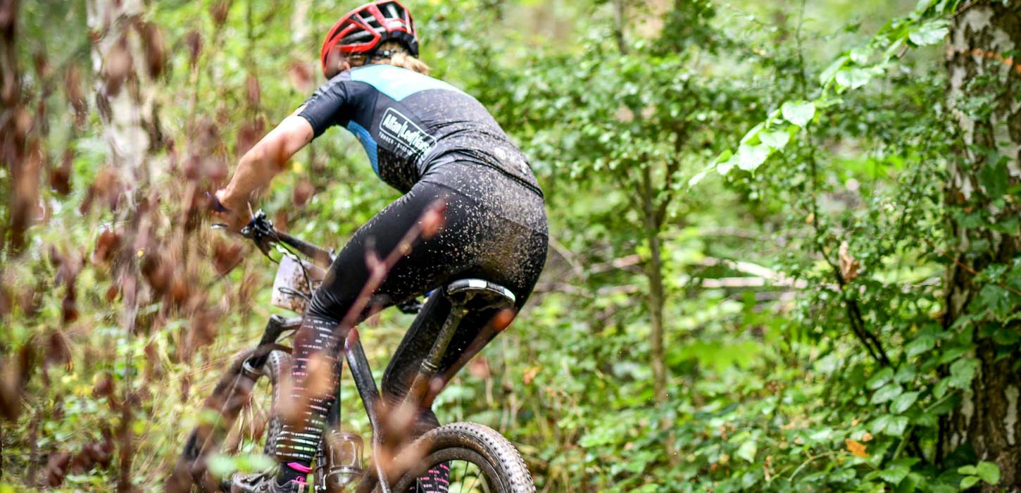 Mountainbiker med rød hjelm er til løb og cykler ude i skoven omringet af en masse grønt.