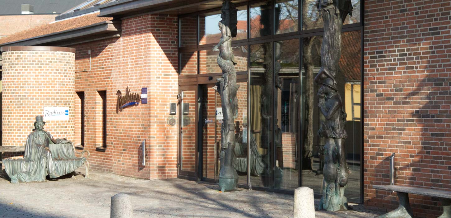 Comwell H.C. Andersens hotel hovedindgang set udefra. Foran hoveddøren ses en statue af HC Andersen, der sidder på en bænk.