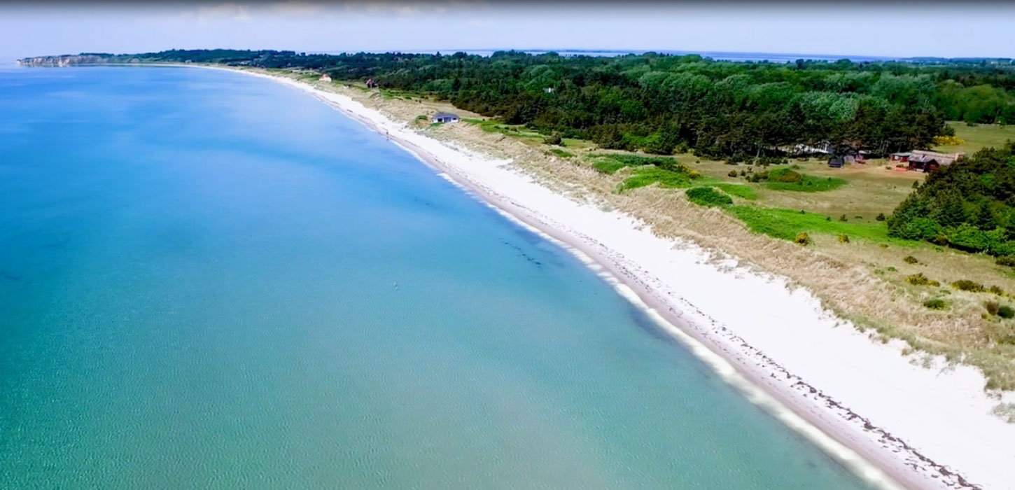 Luftfoto af en hvid sandstrand ud til tyrkisblåt vand