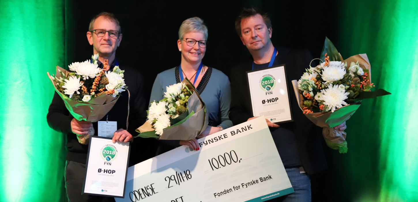 Tre personer med blomster på en scene, der har fået overrakt et gavekort på 10.000 kr.