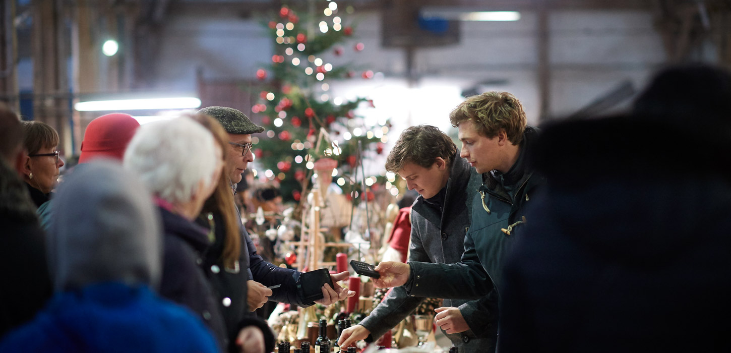 Mennesker, der står og kigger på julesager i boder ved julemarked.