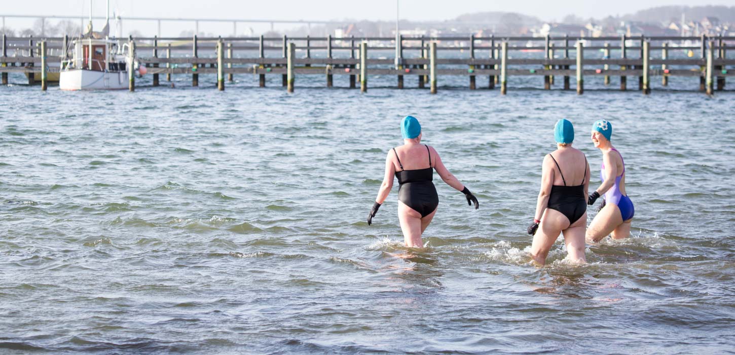 Tre vinterbadere med handsker og hætter på vej ud i vandet.