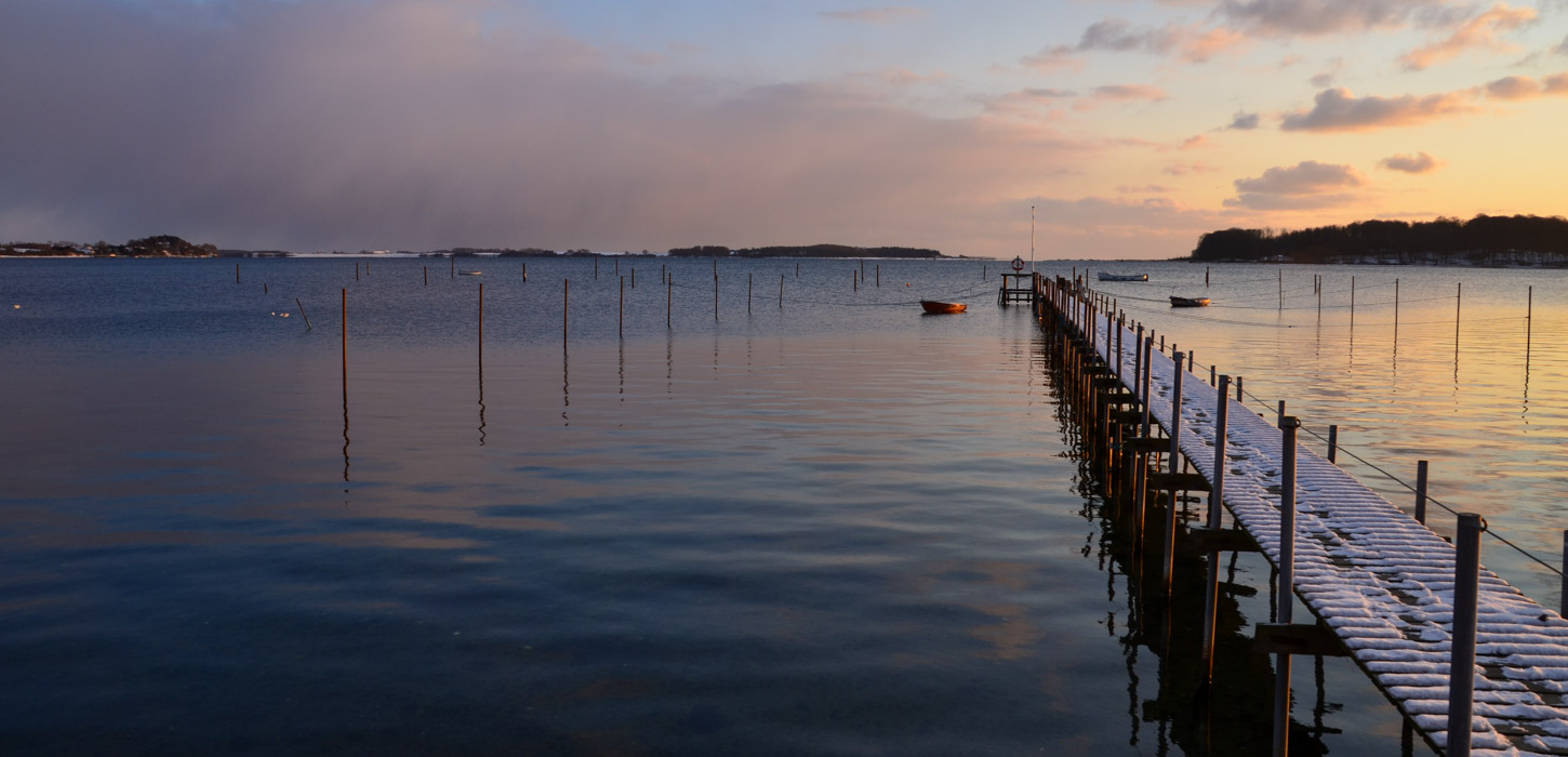 Badebro med fodspor i sneen i solopgangen.