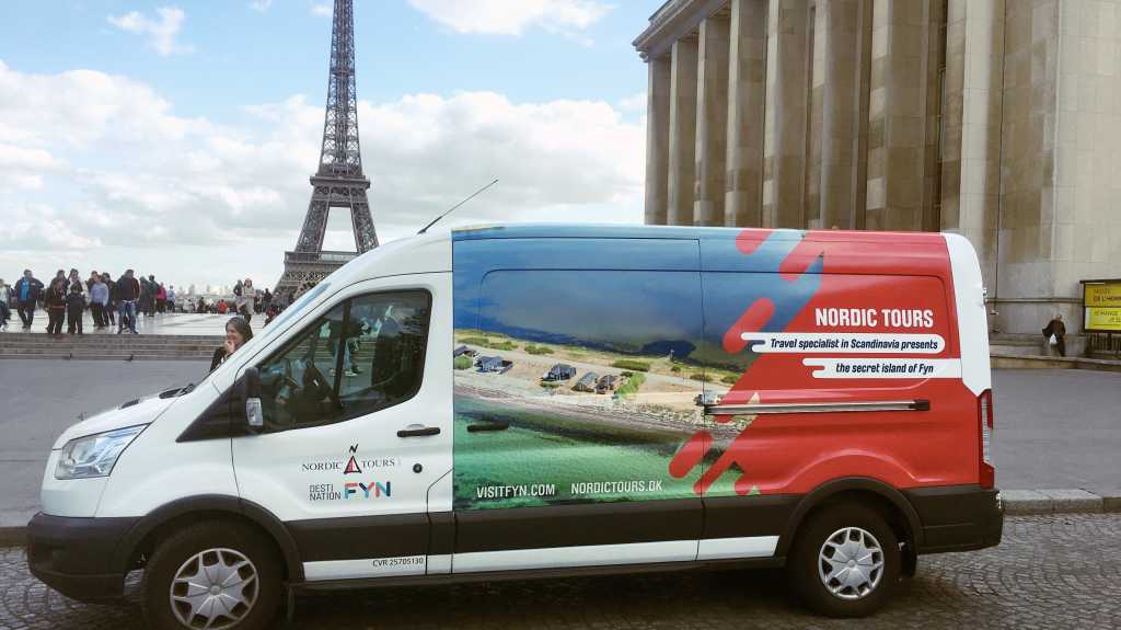 Varevogn holder foran Eiffeltårnet med reklamer på fra Nordic Tours
