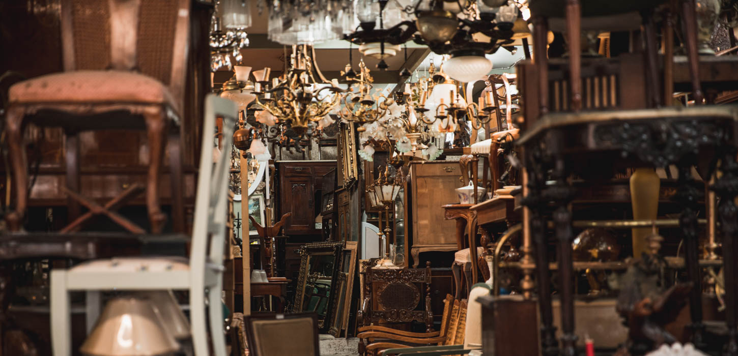 Et mørkt rum er fyldt til randen med antikviteter. Gamle stole, guld lysekroner og gamle lamper.