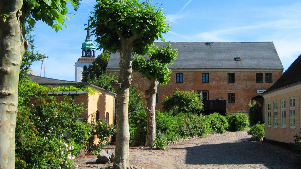 Allé med grønne træer og Andelen Guesthouse-bygningen i baggrunden 