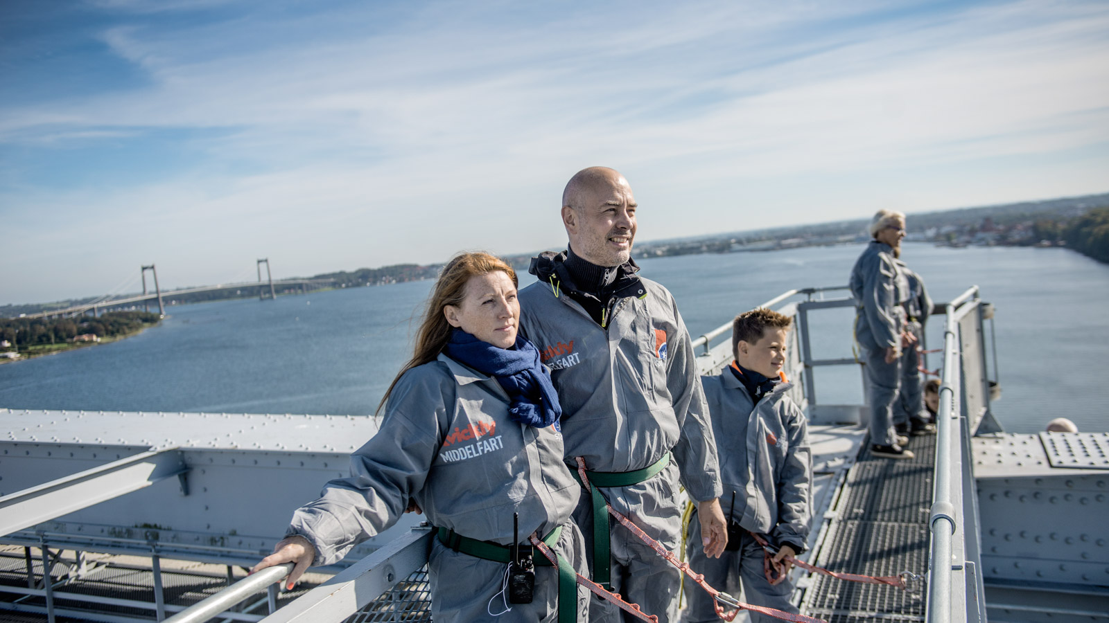Fire mennesker på et gråt stillads. De er på bridgewalking på den gamle Lillebæltsbro. I baggrunden anes den nye Lillebæltsbro.