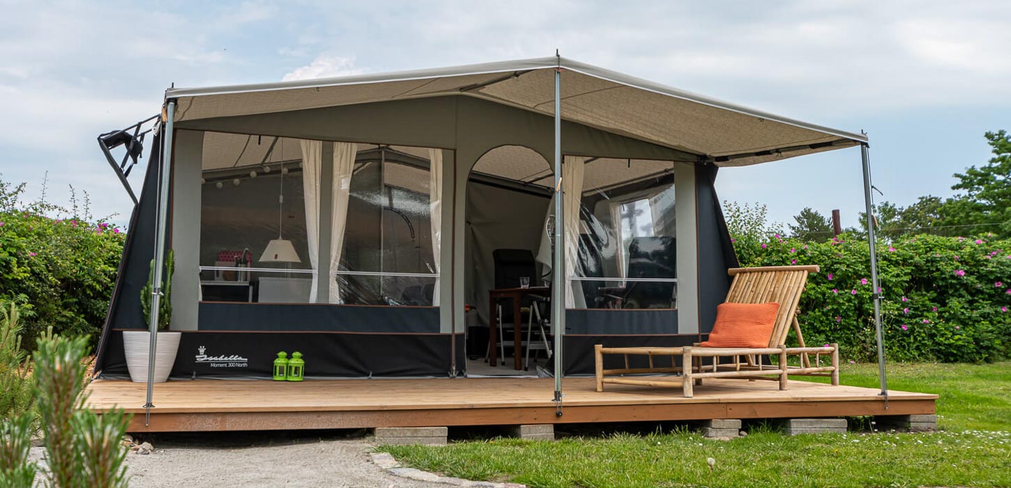 Stort villatelt med træterrasse og liggestol i bambus i grønne omgivelser.