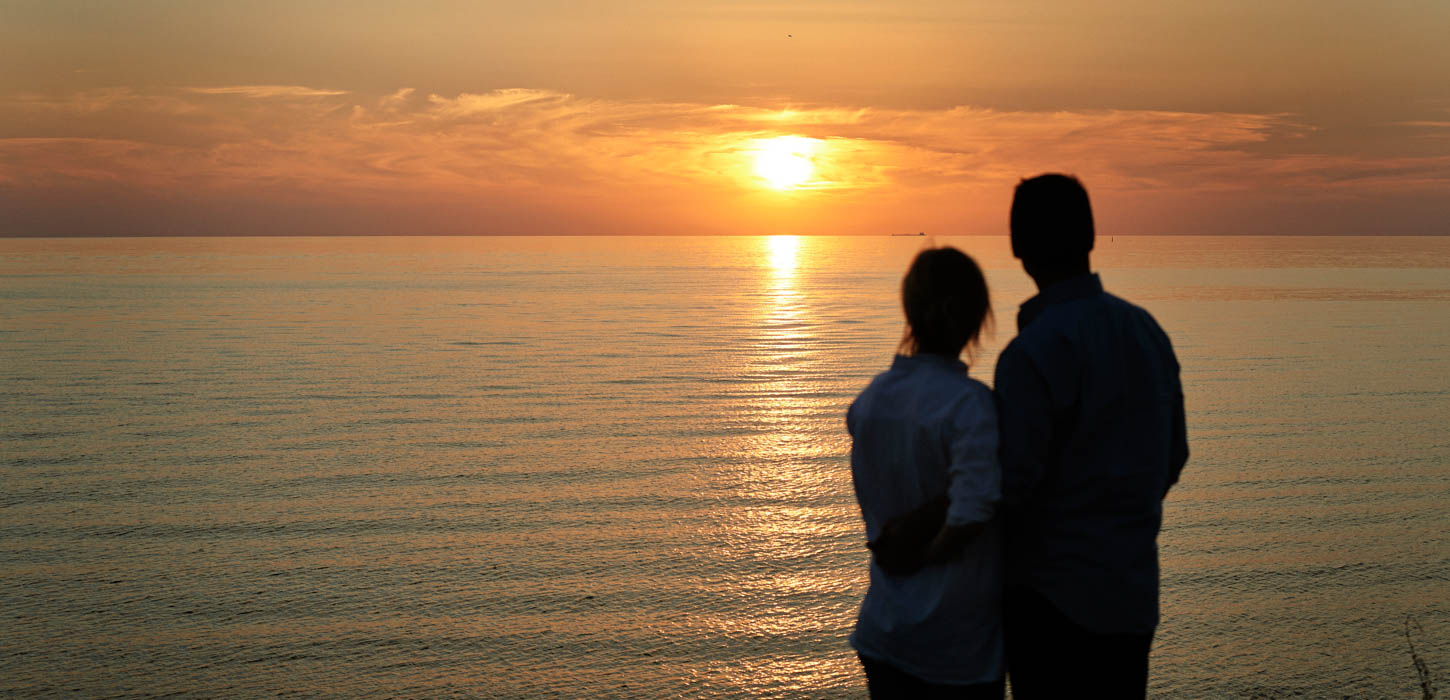 Par står og kigger ud over havet og nyder en flot solnedgang.