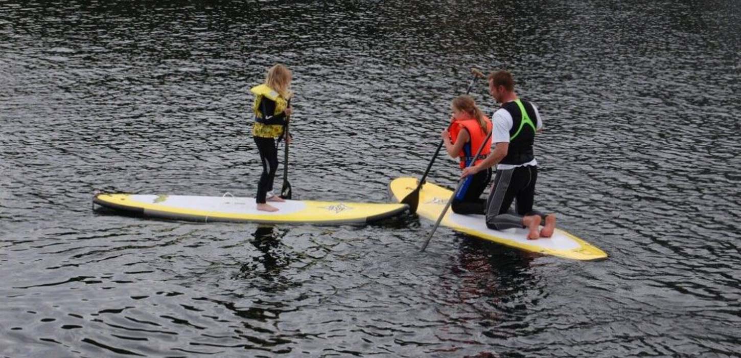 Tre mennesker på stand up paddle boards midt i vandet.