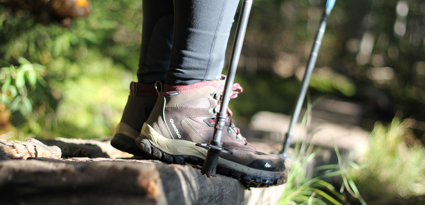 Closeup af en persons vandrestøvler og to vandrestave på en trappe i en skov. 