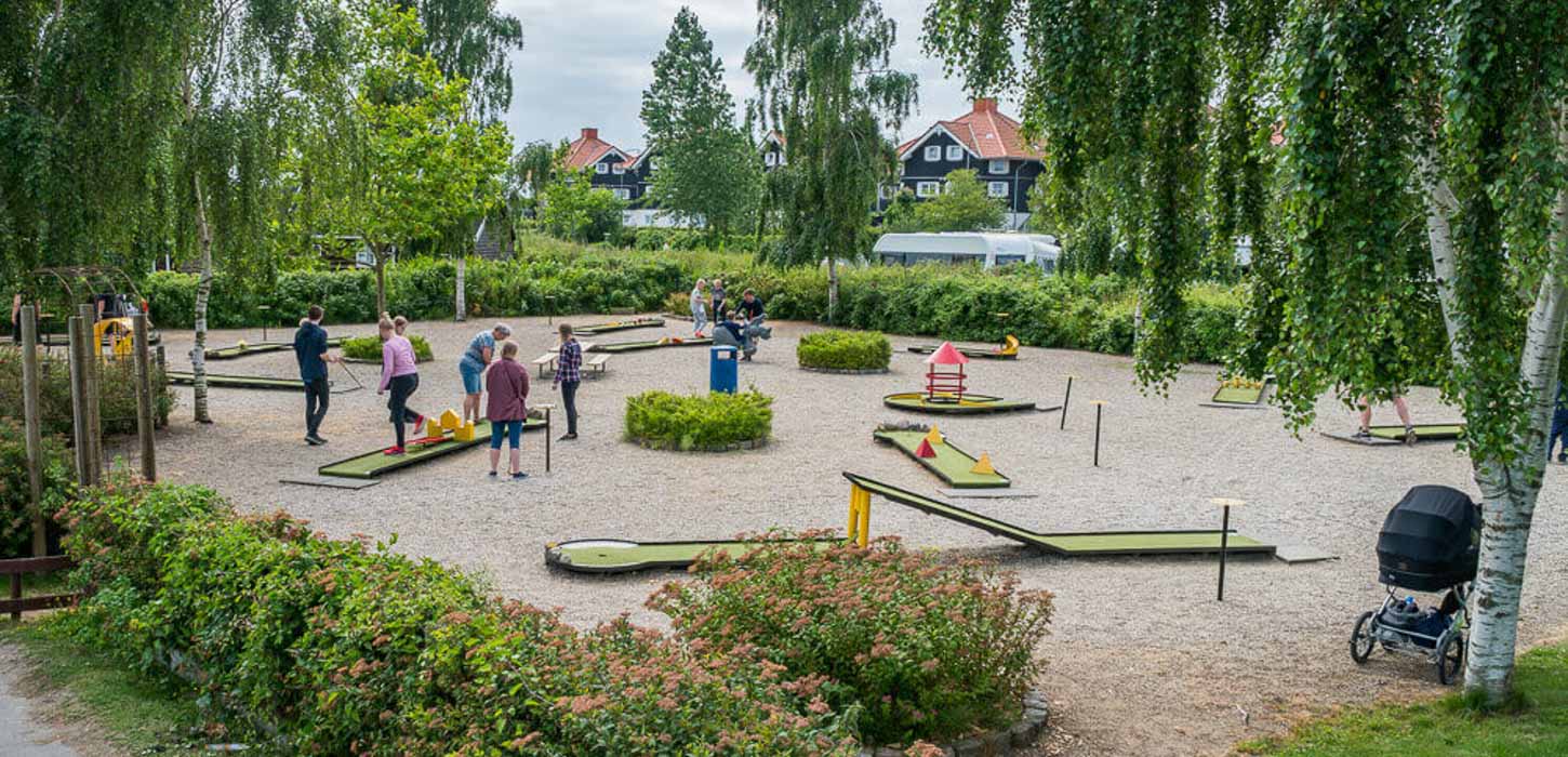 Man ser ind på en minigolfbane. Den består af grus og et flertal af små grønne baner hvor der går folk rundt 