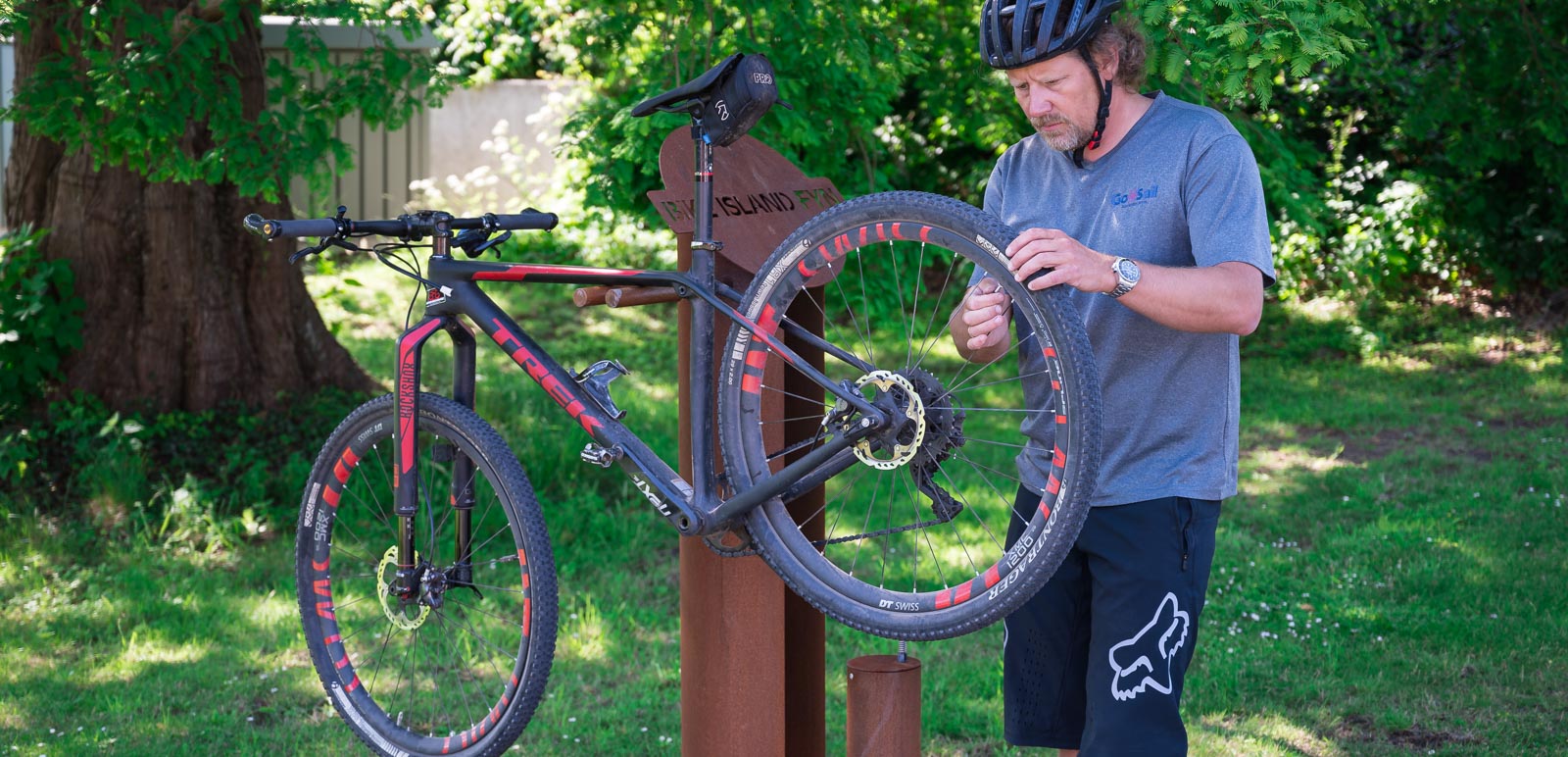Mand med cykelhjelm i færd med at tage bagdækket af sin cykel. Cyklen hænger på et stativ, så den er oppe i en god arbejdshøjde.