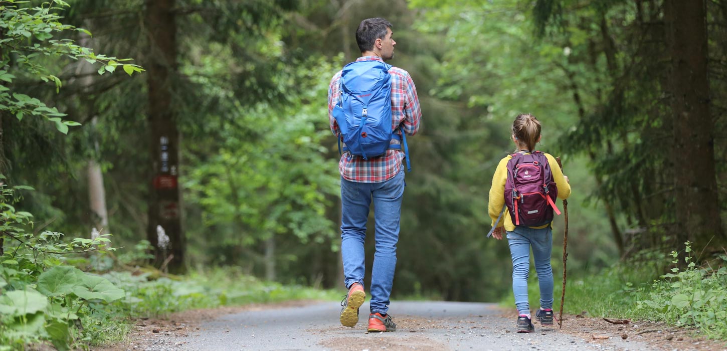 En mand og en pige vandrer med rygsække langs en sti i en grøn skov