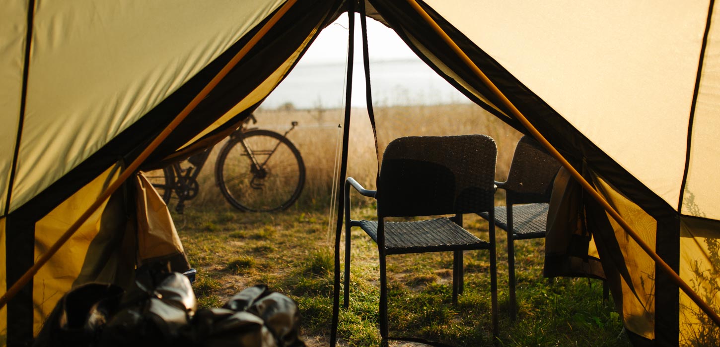 Udsigten fra et telt. To stole er står foran teltet og en cykel holder lidt længere fremme. Man kan en mark og havet.