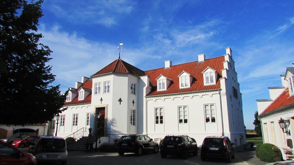 Boltinggaard Gods. Prangende hvid bygning med rødt tegltag mod en skyfri blå himmel.