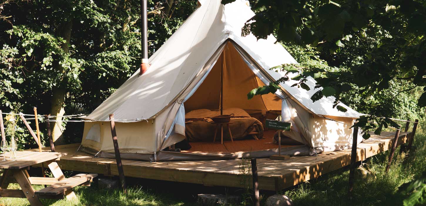 Glampingtelt med lille terasse foran står i grønne naturomgivelser.