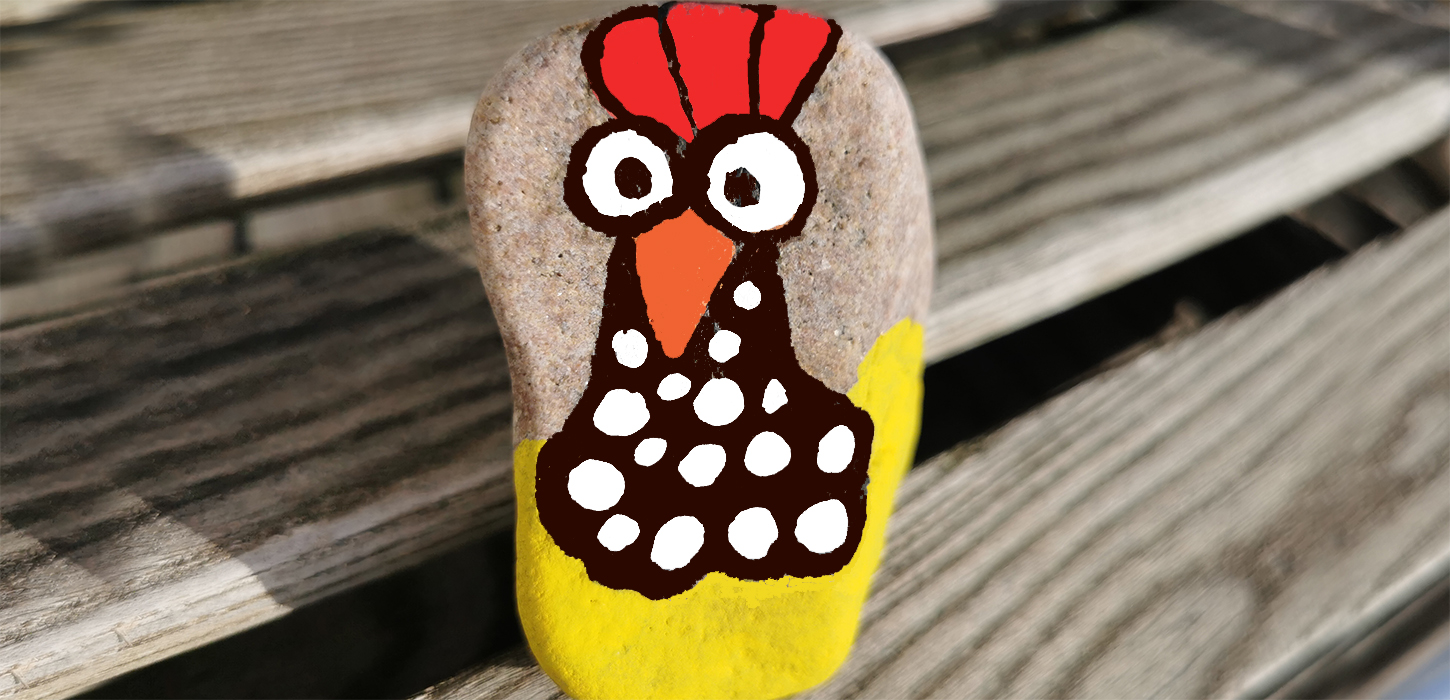 Close-up af en sten, hvor der er malet en høne på i gule, røde, orange, sorte og hvide farver.