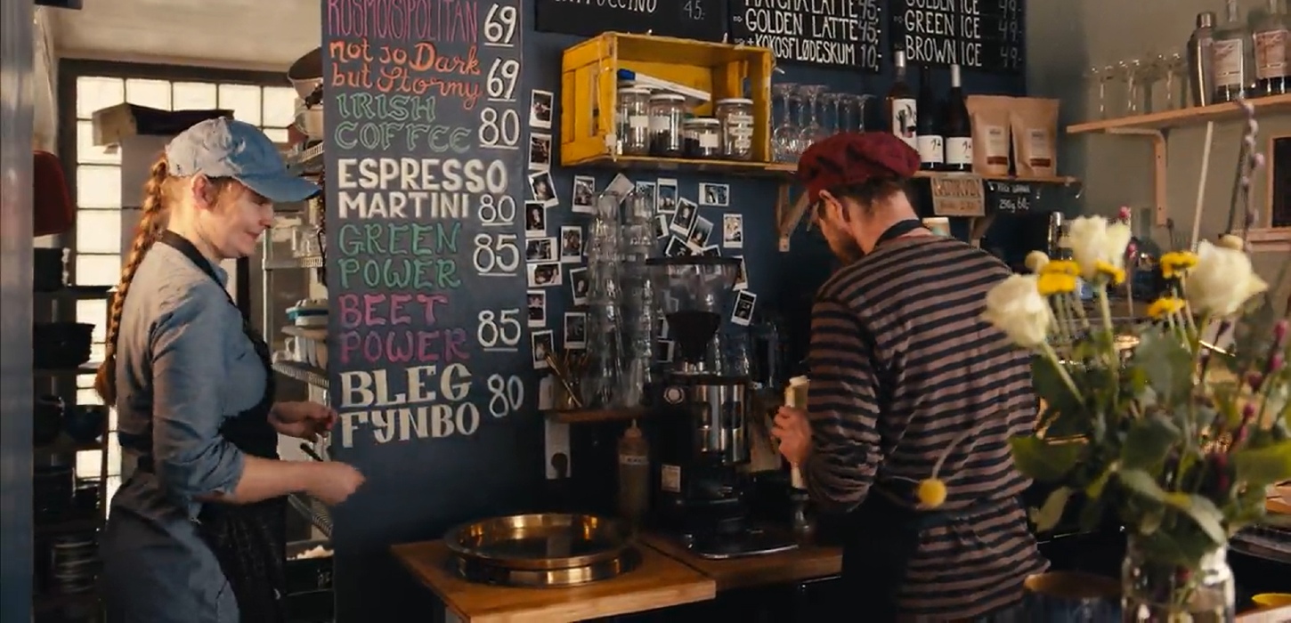 Bag disken på en café står en mand med ryggen til og laver kaffe.