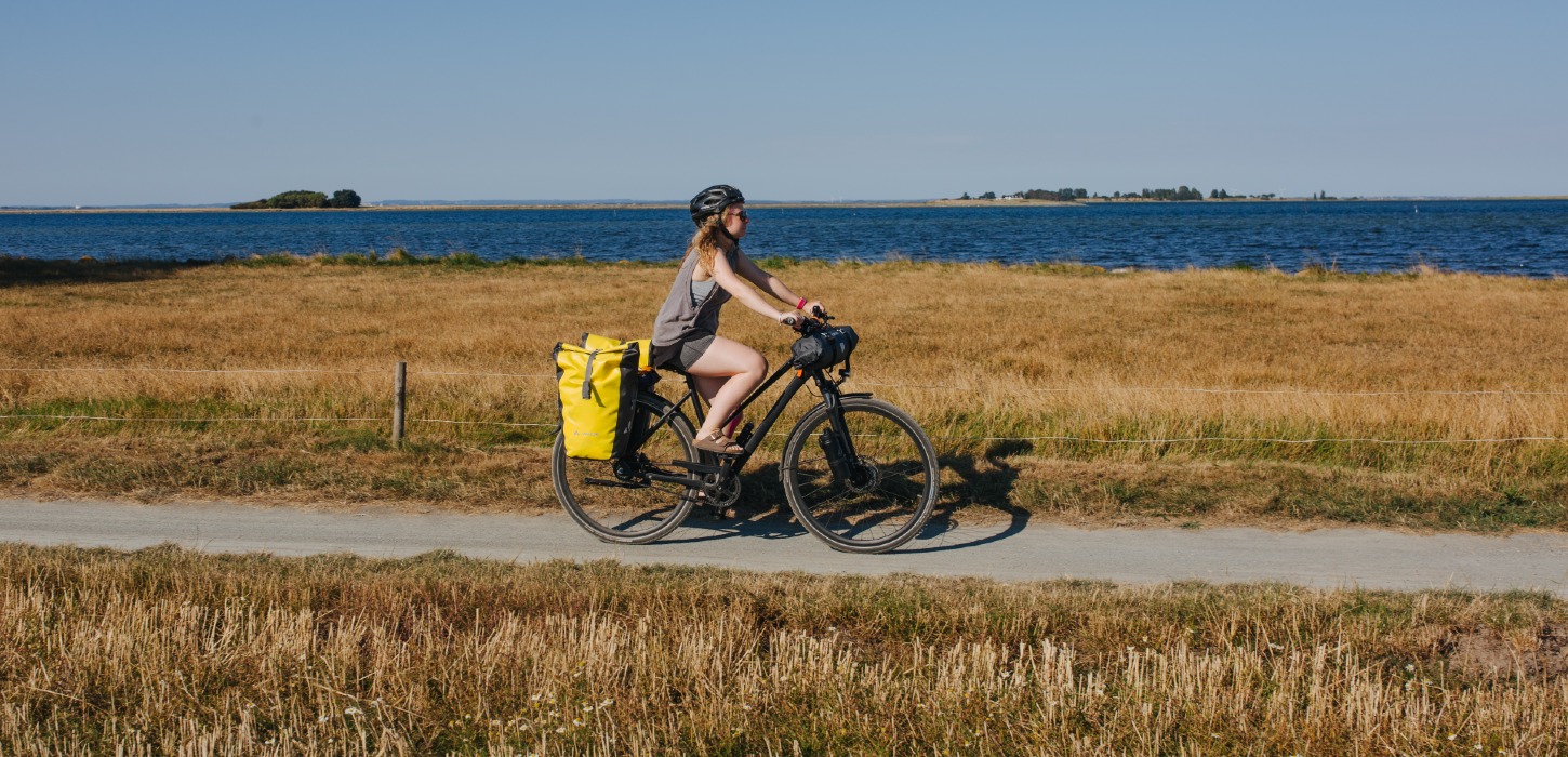 Kvindelig cyklist med oppakning og cykelhjelm på sti ud til havet om sommeren.