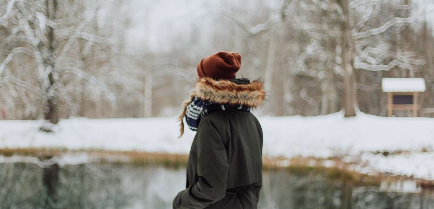 Person står med ryggen til og har en sø med omkringliggende sne foran sig