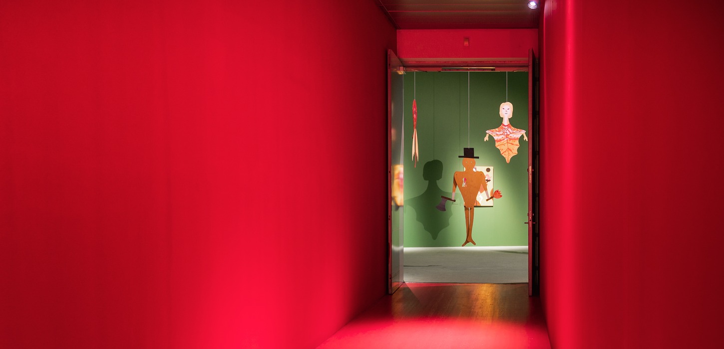 Rødt rum. Gennem et hul i den røde væg ses nogle udstillede genstande, der hænger ned fra loftet foran en grøn væg.