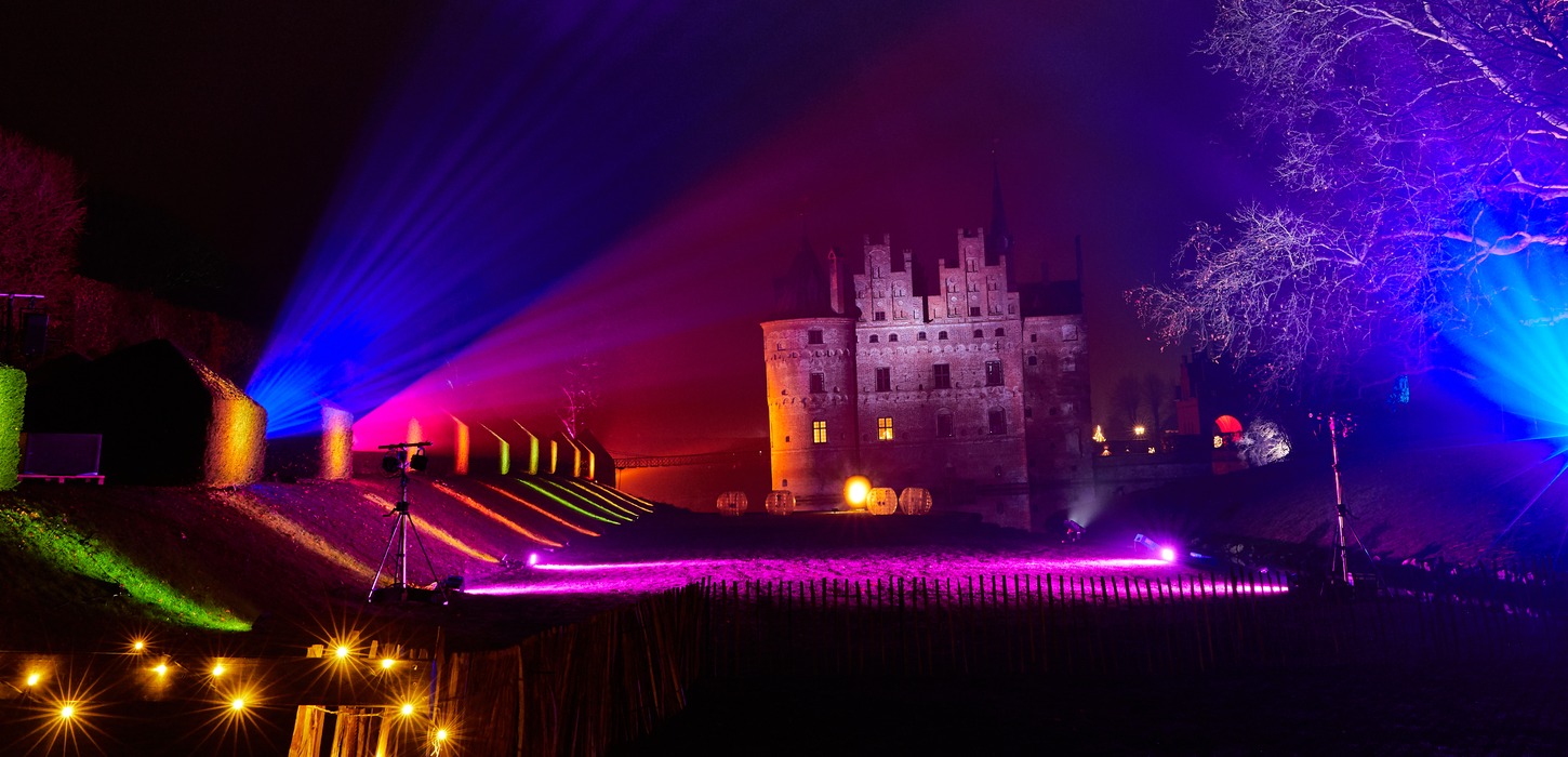 I baggrunden står Egeskov slot i mørket. Den lange græsplæne foran slottet er lyst op af forskellig farvede lamper. 