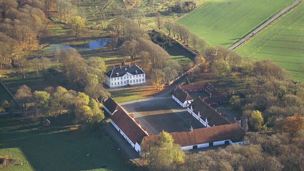 Dronebillede af Hagenskov gods. En hesteskosbygning vender mod selve godset. Bygningerne er omgivet af skov og marker. 