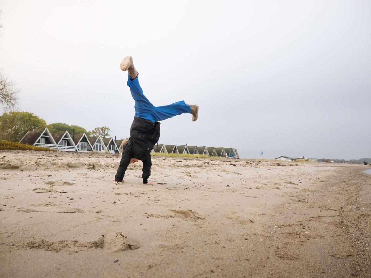 Barn laver vejrmølle på en strand med sommerhuse i baggrunden