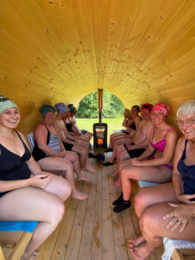 En flok glade mennesker sidder bænket på ræd og række i en træbeklædt sauna