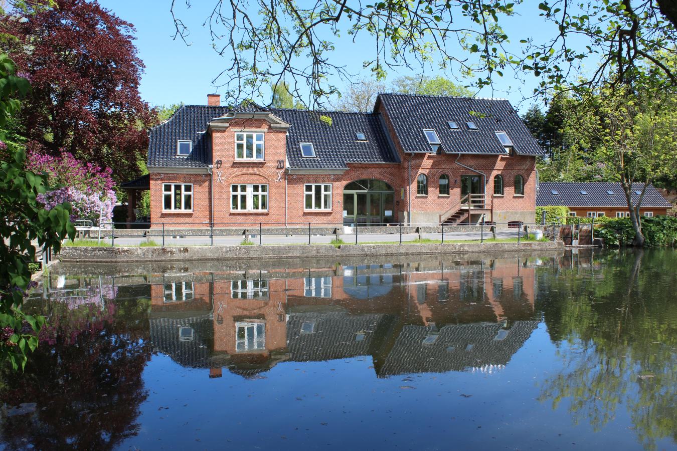 Stort, rødt hus ligger ud til noget vand og spejler sig flot i det. 
