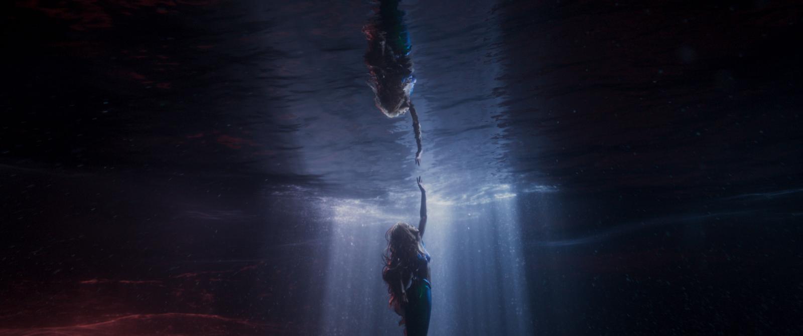 Genspejling af den lille havfrue, der under vandet rækker hånden op mod lyset i vandoverfladen. Scene fra filmen af samme navn.