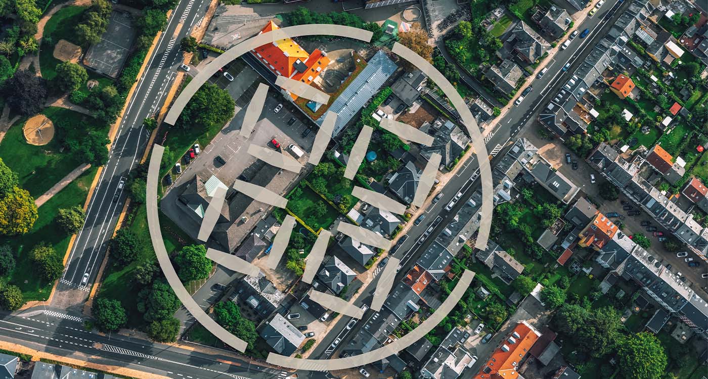 Luftfotografi af en by med grå og røde tage, lige veje og grønne områder.