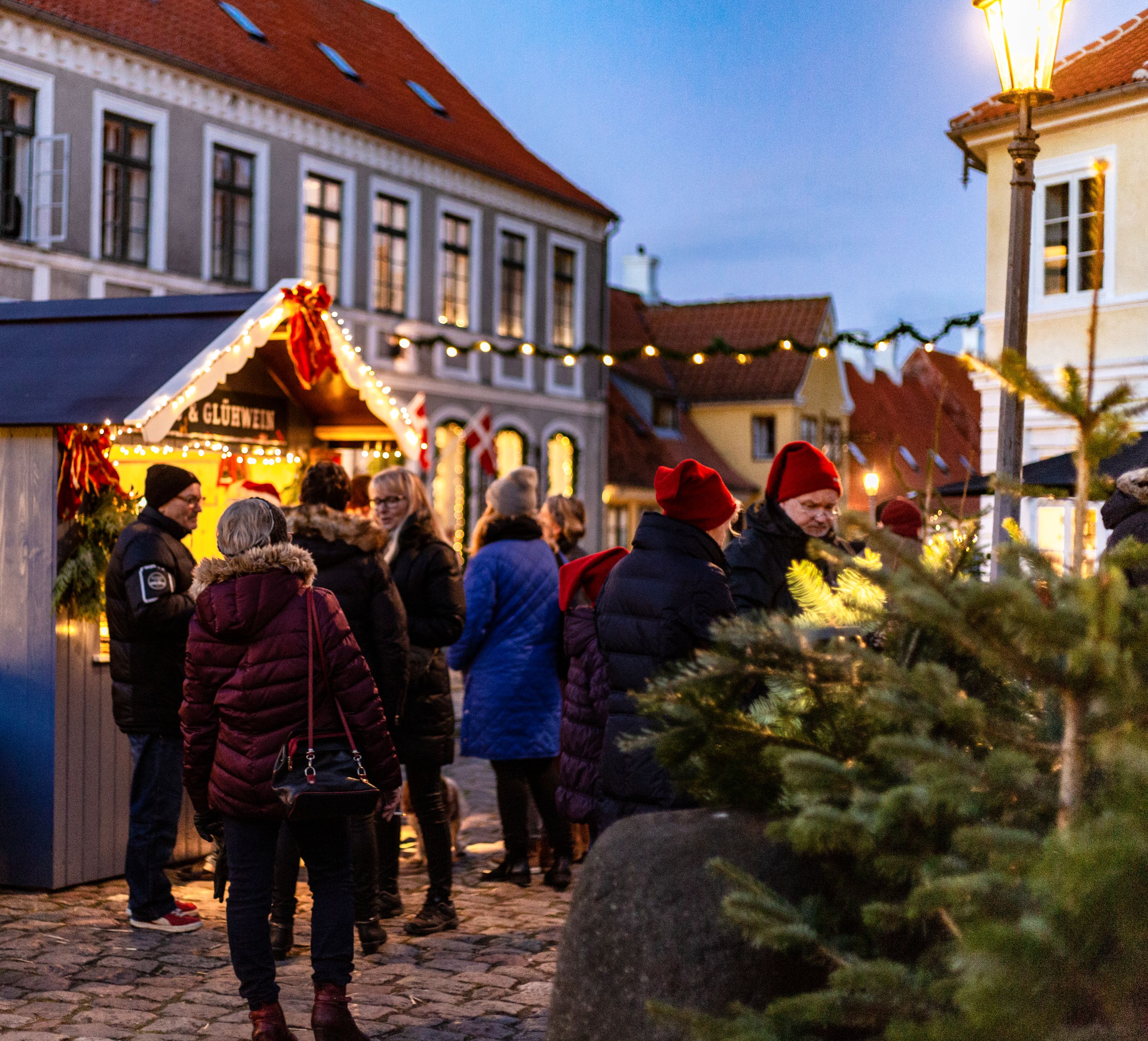 En flok mennesker, der står i en lille by ved en julebod, der sælger glögg 