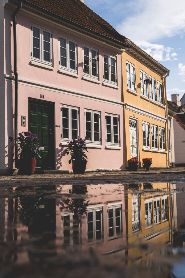 To tætstående huse i smukke farver på en brostensbelagt gade med en kæmpe vandpyt