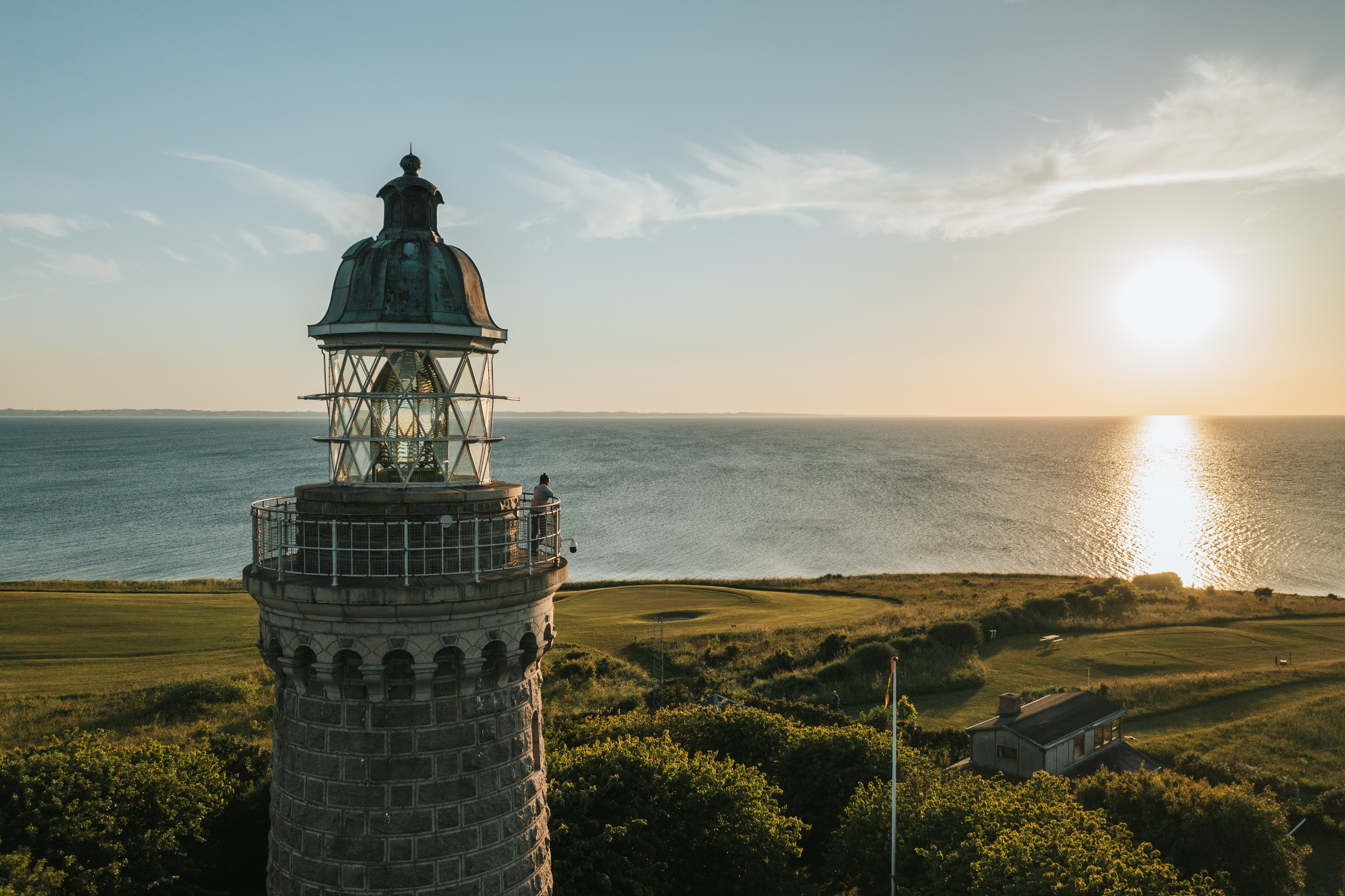Toppen af et fyrtårn på en baggrund af lige dele horisontal himmel, hav og grøn mark