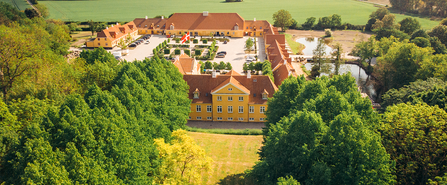 Et dronebillede af Broløkke Herregård med grønne marker og skov