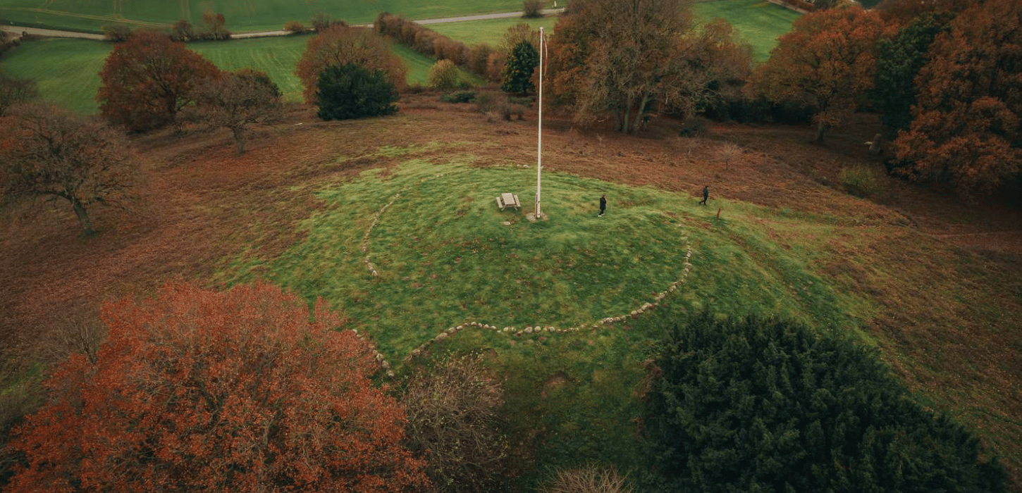 Et billede af en stor bakke set fra luften med en flagstang på toppen